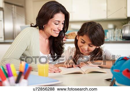 Stock Photo - Mother Helping Daughter With Reading Homework At Table. Fotosearch