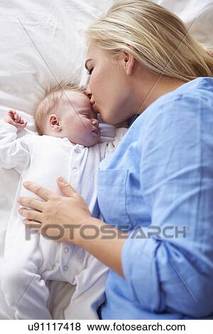 Stock Photo - Mother Kissing Baby Girl As They Lie In Bed Together. Fotosearch