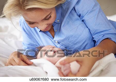 Stock Image - Mother Playing With Baby Girl As They Lie In Bed Together. Fotosearch