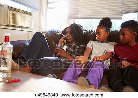 Stock Image - Mother Sits On Sofa With Children Smoking And Drinking. Fotosearch