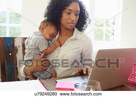 Stock Image - Mother With Baby Working In Office At Home. Fotosearch