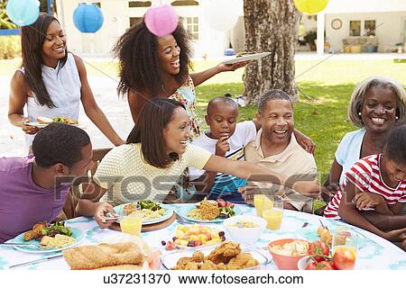 Stock Image - Multi Generation Family Enjoying Meal In Garden Together. Fotosearch