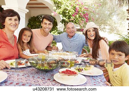 Stock Image - Multi Generation Family Enjoying Meal On Terrace Together. Fotosearch