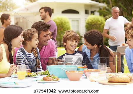 Stock Image - Multi Generation Family Enjoying Meal In Garden Together. Fotosearch