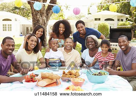 Stock Photo - Multi Generation Family Enjoying Meal In Garden Together. Fotosearch