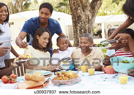Stock Photo - Multi Generation Family Enjoying Meal In Garden Together. Fotosearch