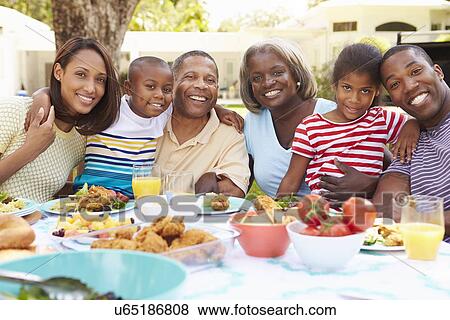 Stock Photo - Multi Generation Family Enjoying Meal In Garden Together. Fotosearch