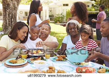 Stock Photo - Multi Generation Family Enjoying Meal In Garden Together. Fotosearch