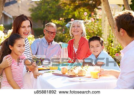 Stock Image - Multi-Generation Family Enjoying Outdoor Meal In Garden. Fotosearch