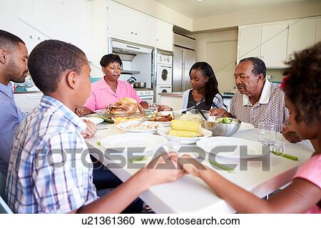 Stock Image - Multi-Generation Family Saying Prayer Before Eating Meal. Fotosearch