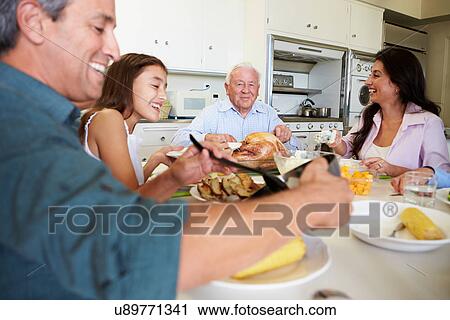 Stock Image - Multi-Generation Family Sitting Around Table Eating Meal. Fotosearch