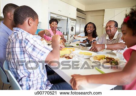 Stock Image - Multi-Generation Family Sitting Around Table Eating Meal. Fotosearch