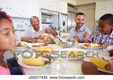 Stock Photography - Multi-Generation Family Sitting Around Table Eating Meal. Fotosearch