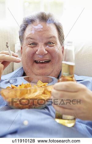 Stock Photo - Overweight Man Eating Chips, Drinking Beer And Smoking. Fotosearch