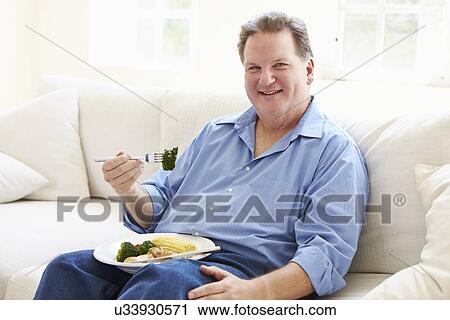 Overweight Man Eating Healthy Meal Sitting On Sofa View Large Photo Image Stock Image - Overweight Man Eating Healthy Meal Sitting On Sofa. Fotosearch