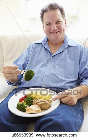 Stock Photo - Overweight Man Eating Healthy Meal Sitting On Sofa. Fotosearch