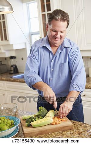 Stock Image - Overweight Man Preparing Vegetables in Kitchen. Fotosearch