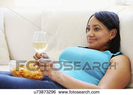 Stock Photograph - Overweight Woman At Home Eating Chips And Drinking Wine. Fotosearch