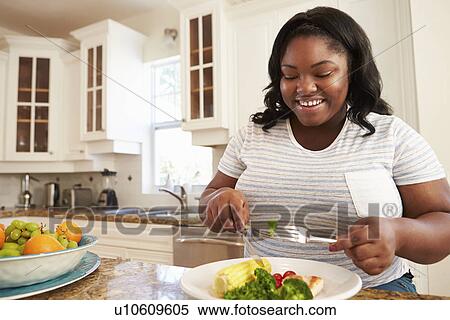 Stock Photography - Overweight Woman Eating Healthy Meal in Kitchen. Fotosearch