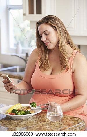 Stock Image - Overweight Woman Eating Healthy Meal And Using Mobile Phone. Fotosearch