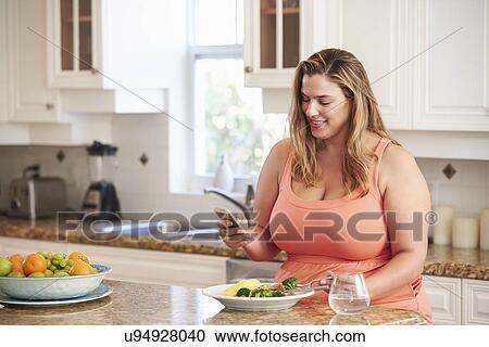 Stock Image - Overweight Woman Eating Healthy Meal And Using Mobile Phone. Fotosearch