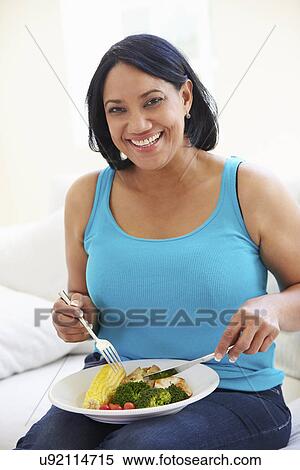 Stock Photography - Overweight Woman Eating Healthy Meal Sitting On Sofa. Fotosearch