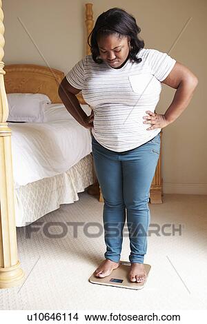 Overweight Woman Weighing Herself On Scales In Bedroom View Large Photo Image Picture - Overweight Woman Weighing Herself On Scales In Bedroom. Fotosearch