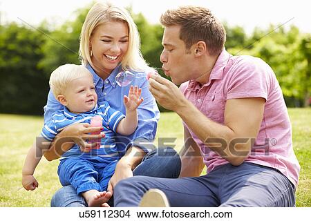 Picture - Parents Blowing Bubbles For Young Boy In Garden. Fotosearch