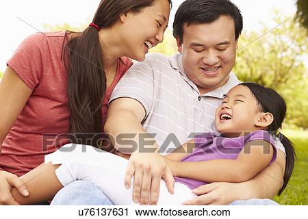 Stock Image - Parents Cuddling Daughter In Park. Fotosearch