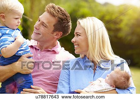 Stock Image - Parents Holding Young Children In Garden. Fotosearch