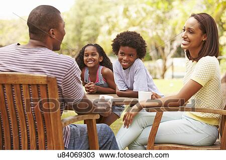 Stock Image - Parents Relaxing Whilst Children Play In Garden . Fotosearch