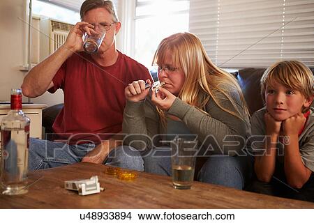Picture - Parents Sit On Sofa With Children Taking Drugs And Drinking. Fotosearch