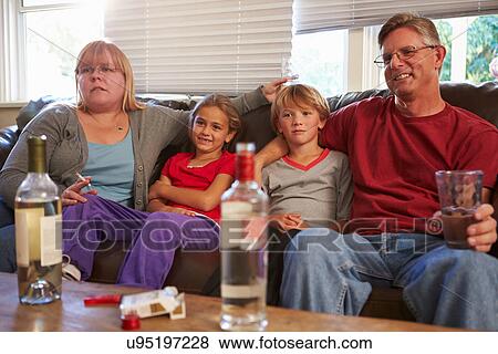 Stock Photo - Parents Sit On Sofa With Children Smoking And Drinking. Fotosearch