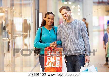 Stock Image - Portrait Of Couple Carrying Bags In Shopping Mall. Fotosearch
