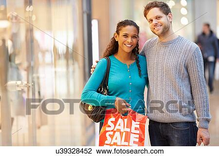 Stock Image - Portrait Of Couple Carrying Bags In Shopping Mall. Fotosearch