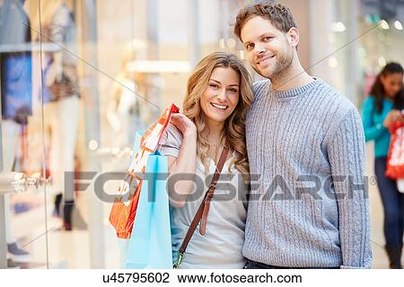 Stock Image - Portrait Of Couple Carrying Bags In Shopping Mall. Fotosearch