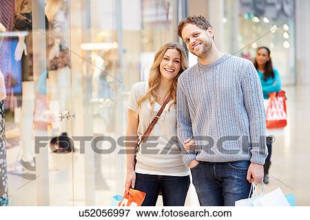 Stock Photo - Portrait Of Couple Carrying Bags In Shopping Mall. Fotosearch