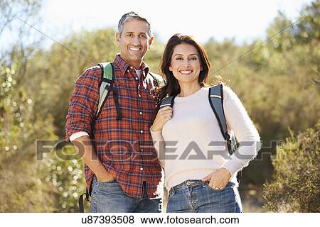Portrait Of Couple Hiking In Countryside Wearing Backpacks View Large Photo Image Stock Photo - Portrait Of Couple Hiking In Countryside Wearing Backpacks. Fotosearch