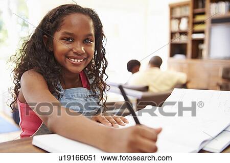 Stock Image - Portrait Of Girl Doing Homework At Table. Fotosearch