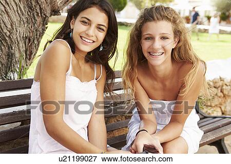 Stock Photo - Portrait Of Two Teenage Girls Sitting On Park Bench Together. Fotosearch
