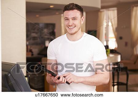 Stock Image - Portrait Of Waiter In Hotel Using Digital Tablet. Fotosearch