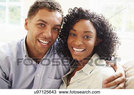 Stock Image - Portrait Of Young Couple Sitting On Sofa At Home. Fotosearch