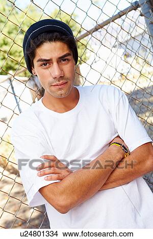 Picture - Portrait Of Young Man In Urban Setting Standing By Fence. Fotosearch