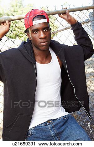 Stock Image - Portrait Of Young Man In Urban Setting Standing By Fence. Fotosearch
