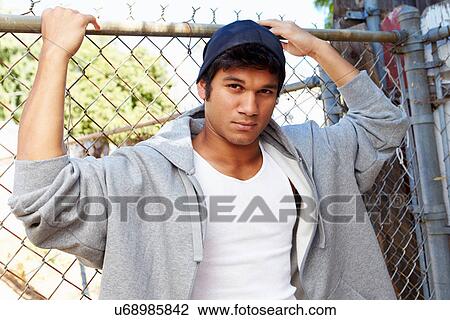 Stock Image - Portrait Of Young Man In Urban Setting Standing By Fence. Fotosearch