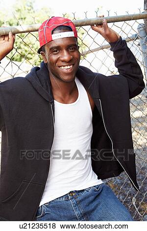 Stock Photo - Portrait Of Young Man In Urban Setting Standing By Fence. Fotosearch