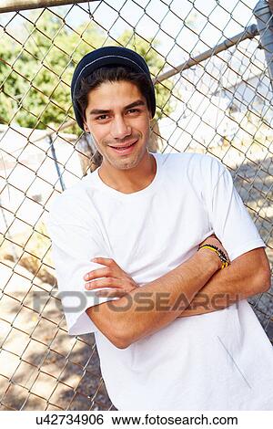 Stock Photograph - Portrait Of Young Man In Urban Setting Standing By Fence. Fotosearch