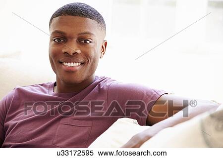 Stock Photography - Portrait Of Young Man Relaxing Sitting On Sofa. Fotosearch