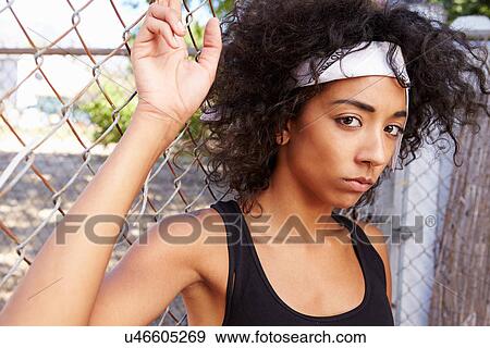 Portrait Of Young Woman In Urban Setting Standing By Fence View Large Photo Image Stock Photo - Portrait Of Young Woman In Urban Setting Standing By Fence. Fotosearch