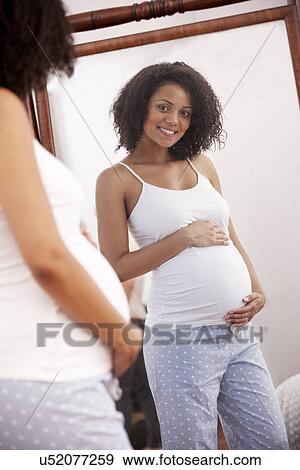 Stock Photo - Pregnant woman looking in mirror. Fotosearch